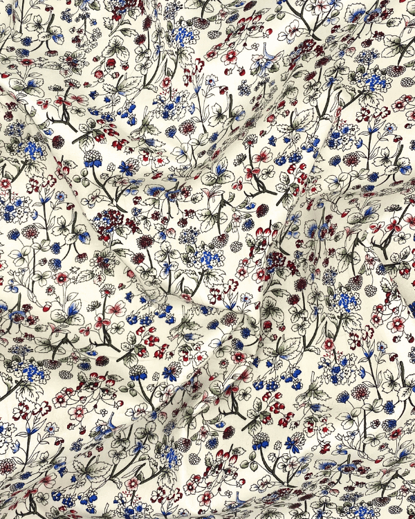 Draped view of cream floral cotton fabric with red and blue flowers, showcasing fabric drape, softness, and movement.