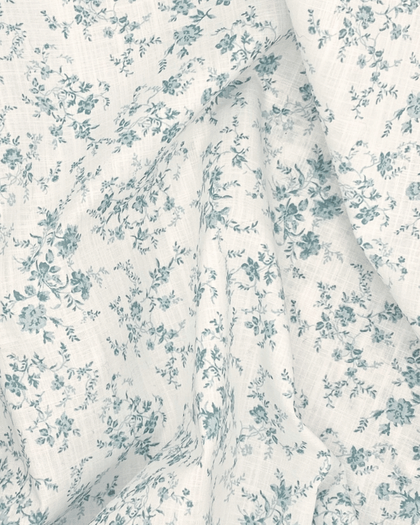 Soft and airy green floral cotton slub fabric with a touch of light blue, draped to showcase lightweight texture and vintage-inspired design, perfect for dresses and home décor.